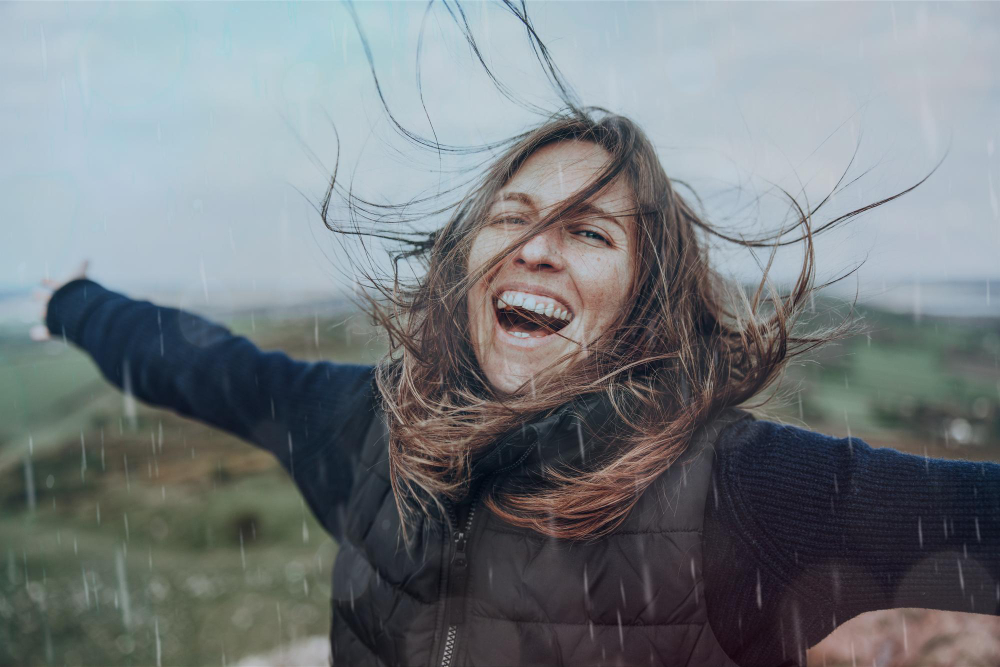 Mulher sorrindo de braços abertos na chuva